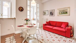 A dining area with a round table, white chairs, and a red sofa.