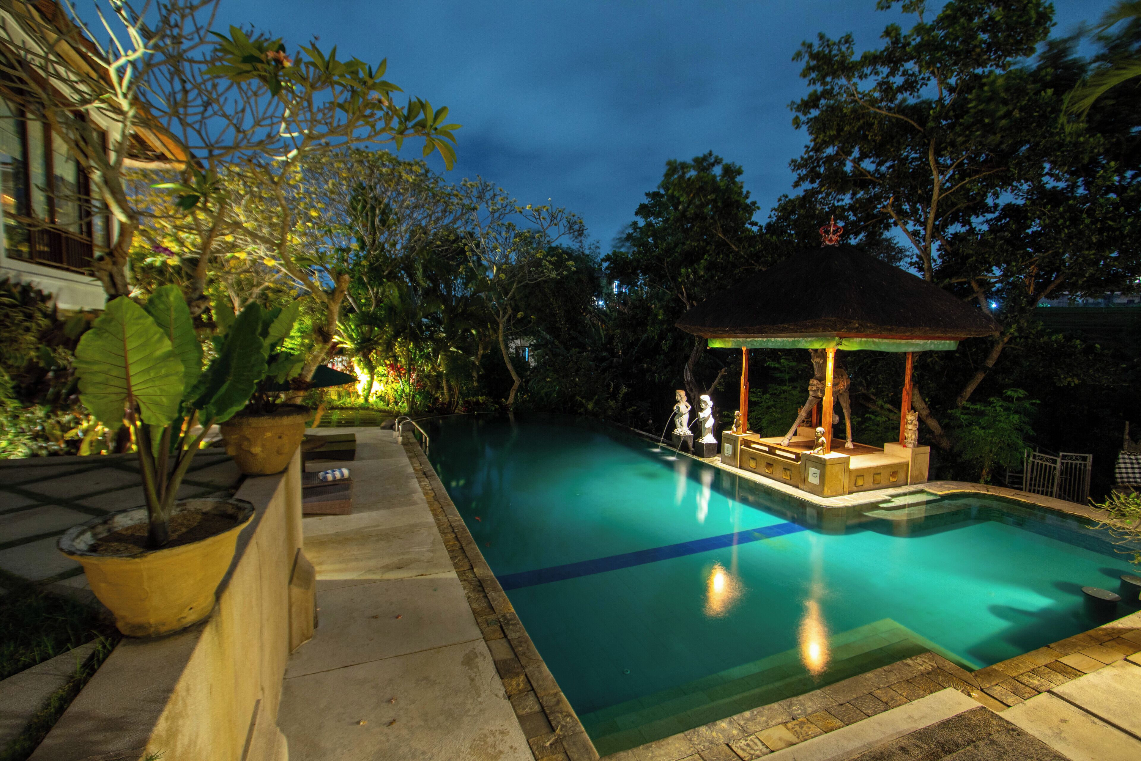 A swimming pool with a gazebo, surrounded by potted plants and trees.