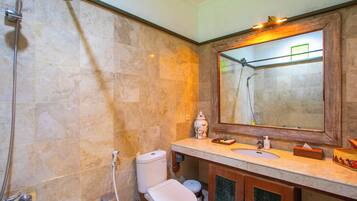 A bathroom with a marble wall, a wooden vanity, a large mirror, a toilet, and a shower.