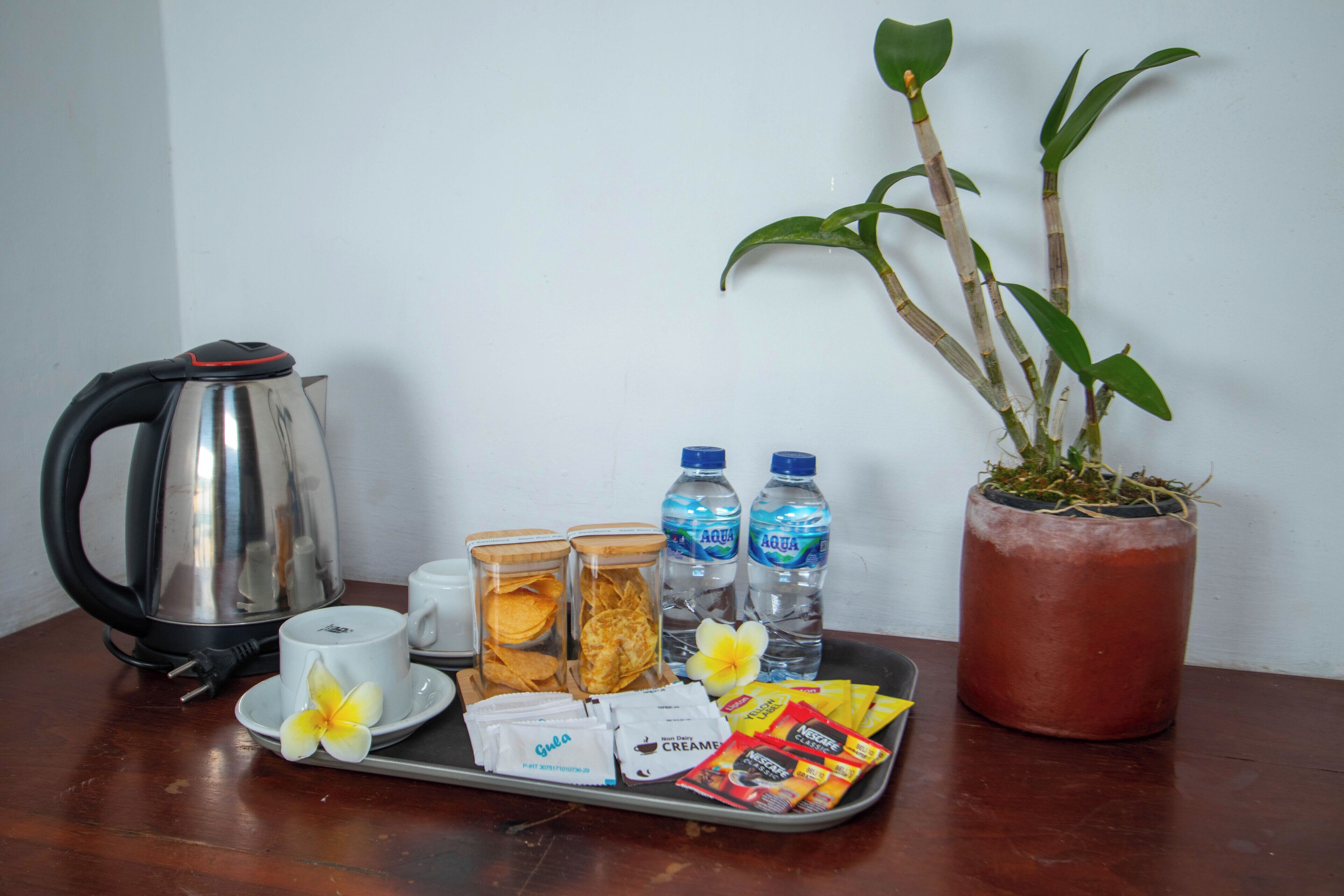 A tray with a kettle, cups, snacks, and water bottles on a wooden table.