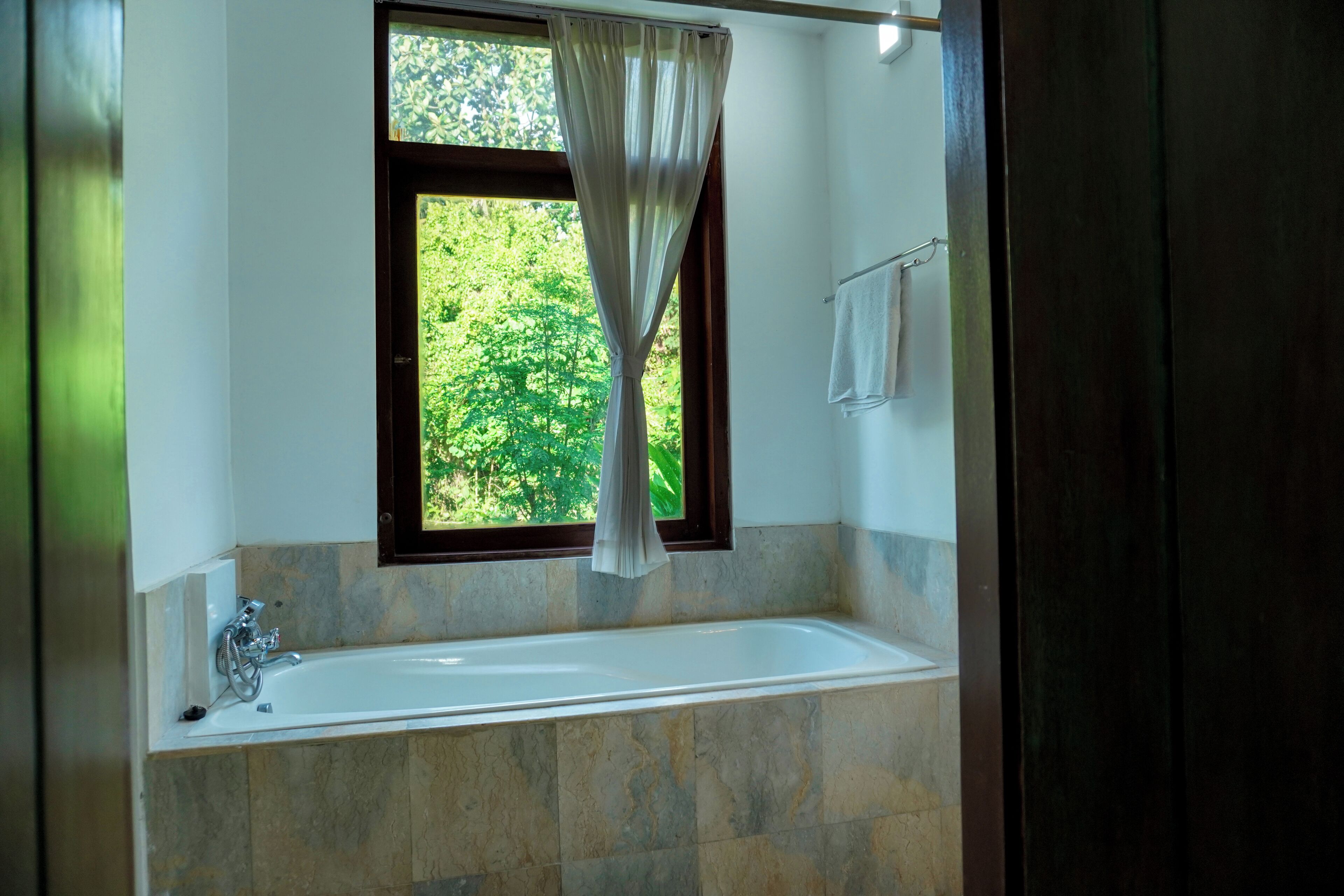 A bathroom with a bathtub, a window with a curtain, and a towel rack.