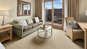 Ein Wohnzimmer mit einem grünen Sofa, einem runden Couchtisch, einem Korbstuhl und einer großen Glastür, die zu einem Außenbereich führt.