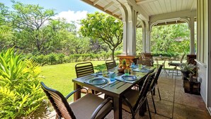 An outdoor patio with a table set for dining, surrounded by chairs, and a view of a lush garden.