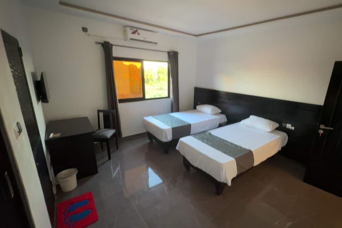 A hotel room with two single beds, a desk with a chair, a small table, a TV, and a door marked '205'.
