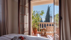 Une chambre avec un lit, un plateau avec des tasses et une théière, et un balcon avec une table et des chaises.