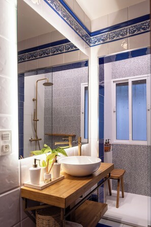 Een moderne badkamer met een grote spiegel, een houten wastafelmeubel, een witte wasbak en een douchehoek.