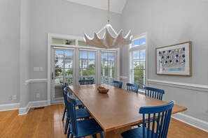 A dining room with a wooden table, blue chairs, a chandelier, and a framed picture on the wall.