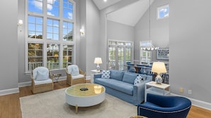 A spacious living room with a large window, a blue sofa, a round coffee table, and a dining area with blue chairs.