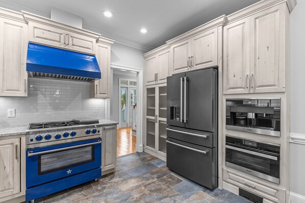 A kitchen with white cabinets, a blue oven, a black refrigerator, and a built-in oven.