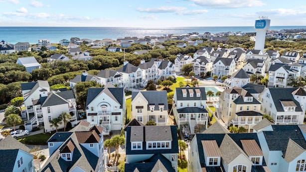 A coastal residential area with houses, a prominent water tower, and a view of the ocean.