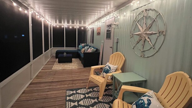 A covered outdoor deck with string lights, wooden flooring, and seating arrangements. - Absolutely Darling private little oasis !  (Holly Ridge)