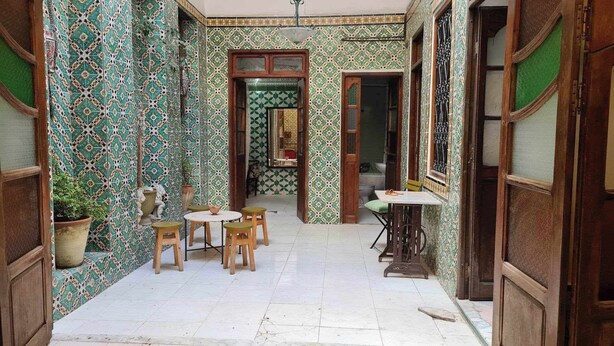 A narrow hallway with patterned tiles, a small round table with chairs, and a window with a view. - Atelier D (Tunis)