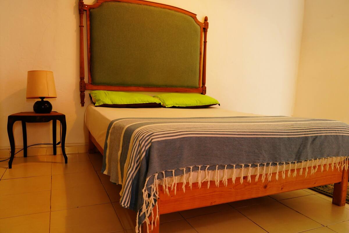 A neatly made bed with a wooden frame, a green headboard, and a striped blanket.