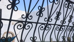 A wrought iron gate with a view of a tiled patio area, potted plants, and a yellow sign with text. - Atelier D (Tunis)