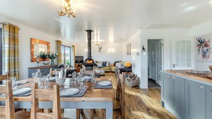 A spacious living area with a dining table set for four, a fireplace, and a kitchen with grey cabinets. - Towford Farm Bungalow (Jedburgh)