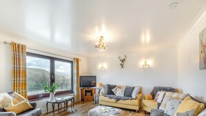 A cozy living room with a large window, a flat-screen TV, and a fireplace. - Towford Farm Bungalow (Jedburgh)
