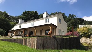 A two-story house with a porch and a wooden fence. - Quiet and secluded farmhouse, with far reaching views, spacious and comfortable  (Liskeard)
