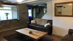 A cozy living room with a stone wall, a brown leather sofa, a wooden coffee table, and a staircase leading to an upper level. - Quiet and secluded farmhouse, with far reaching views, spacious and comfortable  (Liskeard)