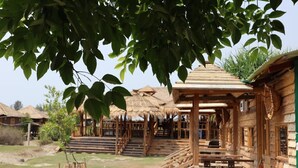 A wooden structure with a thatched roof, a staircase leading to a porch, and a view of other similar buildings in the background. - Sinbad Beach Resort (Saint Martin's Island)
