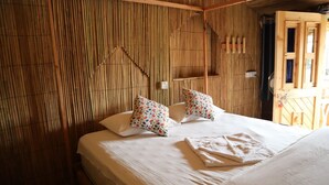A room with a bed, two pillows, a bedside table, and a wall with vertical bamboo slats. - Sinbad Beach Resort (Saint Martin's Island)