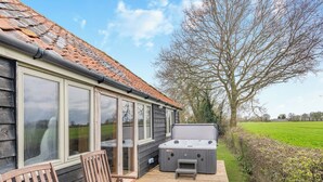 A wooden deck with a hot tub, two wooden chairs, and a large window overlooking a green field. - 2 bedroom accommodation in Fressingfield, near Eye (Fressingfield, near Eye)