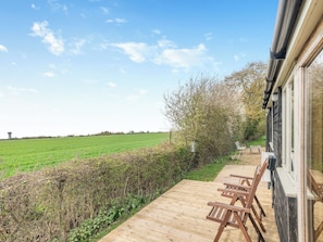 A wooden deck with chairs, a view of a green field, and a building with a window.