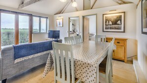 A room with a high ceiling, wooden beams, a dining table with chairs, a sofa, a television, and a painting on the wall. - 2 bedroom accommodation in Fressingfield, near Eye (Fressingfield, near Eye)