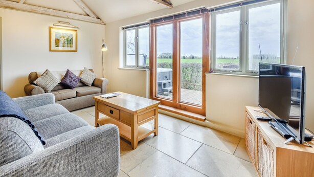 A living room with a sofa, a coffee table, a TV, and large windows with a view of the countryside. - 2 bedroom accommodation in Fressingfield, near Eye (Fressingfield, near Eye)