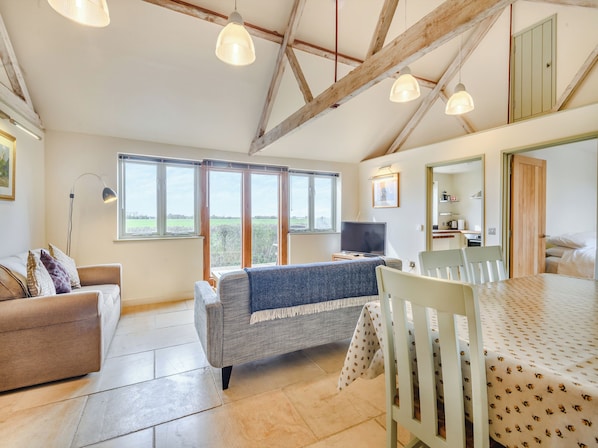 A spacious room with a high ceiling, large windows, a dining table, a sofa, and a television.