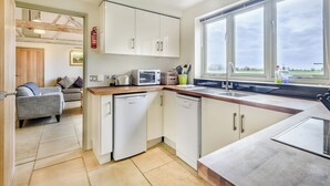 A modern kitchen with white cabinets, a dishwasher, a microwave, and a large window offering a view of the outdoors. - 2 bedroom accommodation in Fressingfield, near Eye (Fressingfield, near Eye)