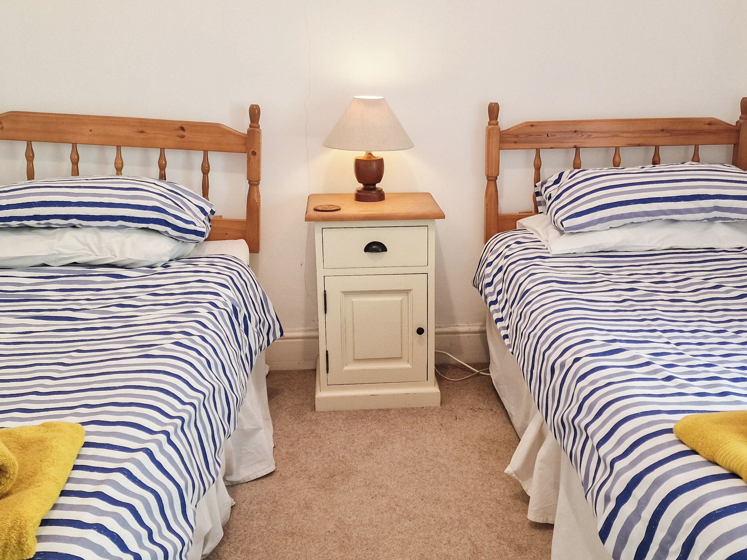 Une chambre avec deux lits, une table de chevet avec une lampe et une tête de lit en bois.