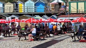 A beachside area with wooden benches and red umbrellas, surrounded by colorful beach huts.