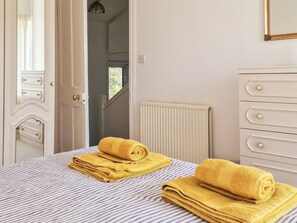 A hotel room with a bed, a radiator, a white dresser, and a door leading to another room.
