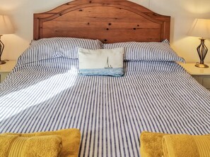 A bed with striped bedding, a wooden headboard, and two bedside lamps. - A wonderful holiday cottage close to the beach and town centre of Beer. (Beer)