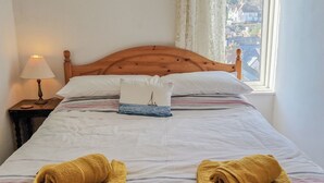 A neatly made bed with a wooden headboard, white linens, and two rolled towels.