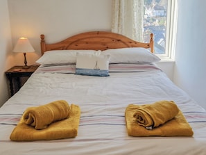 A neatly made bed with a wooden headboard, white linens, and two rolled towels.