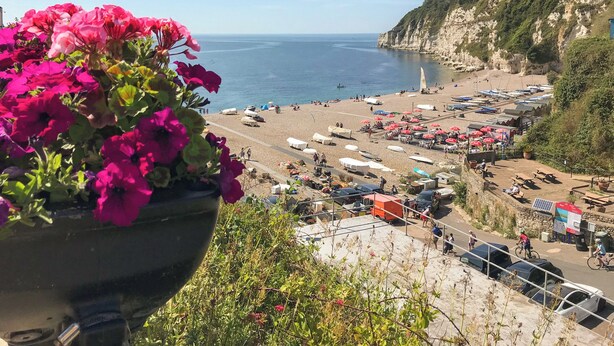 A coastal beach scene with tents, boats, and a cliffside.