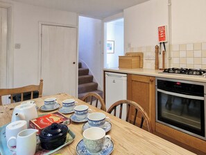 A kitchen with a dining table set for tea, a stove, oven, and a staircase leading to another room. - A wonderful holiday cottage close to the beach and town centre of Beer. (Beer)