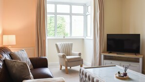 A living room with a sofa, armchair, ottoman, TV, and a window with curtains.