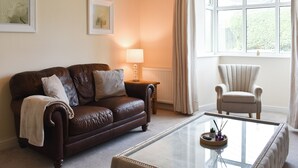 A living room with a brown leather sofa, a beige armchair, a glass coffee table, and two framed pictures on the wall.