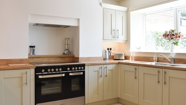 A modern kitchen with a Kenwood oven, light-colored cabinets, a wooden countertop, and a window with a view.