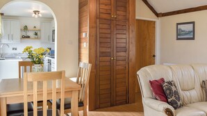 A dining area with a wooden table and chairs, a kitchen in the background, and a beige sofa with decorative pillows. - 2 bedroom accommodation in Criccieth (Criccieth)