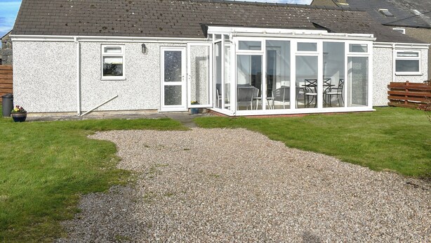 A house with a covered patio, a gravel driveway, and a grassy lawn. - 2 bedroom accommodation in Criccieth (Criccieth)