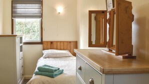 A bedroom with a bed, a dresser, a mirror, and a window with blinds. - 2 bedroom accommodation in Criccieth (Criccieth)