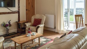 A living room with a wooden ceiling, a sofa, a coffee table, a chair, a radiator, and a TV mounted on the wall. - 2 bedroom accommodation in Criccieth (Criccieth)