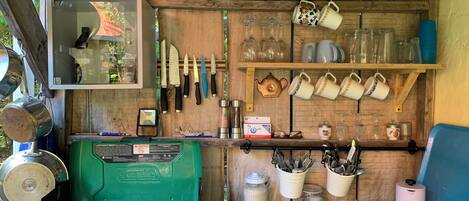 A rustic kitchen with a propane stove, hanging knives, and various kitchen utensils.
