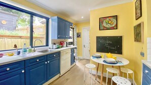 Een compacte keuken met blauwe kastjes, een wit aanrecht en een prikbord met een welkomstboodschap.