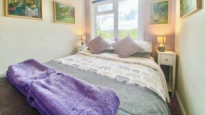 Een slaapkamer met een bed, twee nachtkastjes, een raam en drie schilderijen aan de wand.