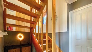 Een houten trap met een leuning, een lamp aan de muur en een deur met decoratief paneel.