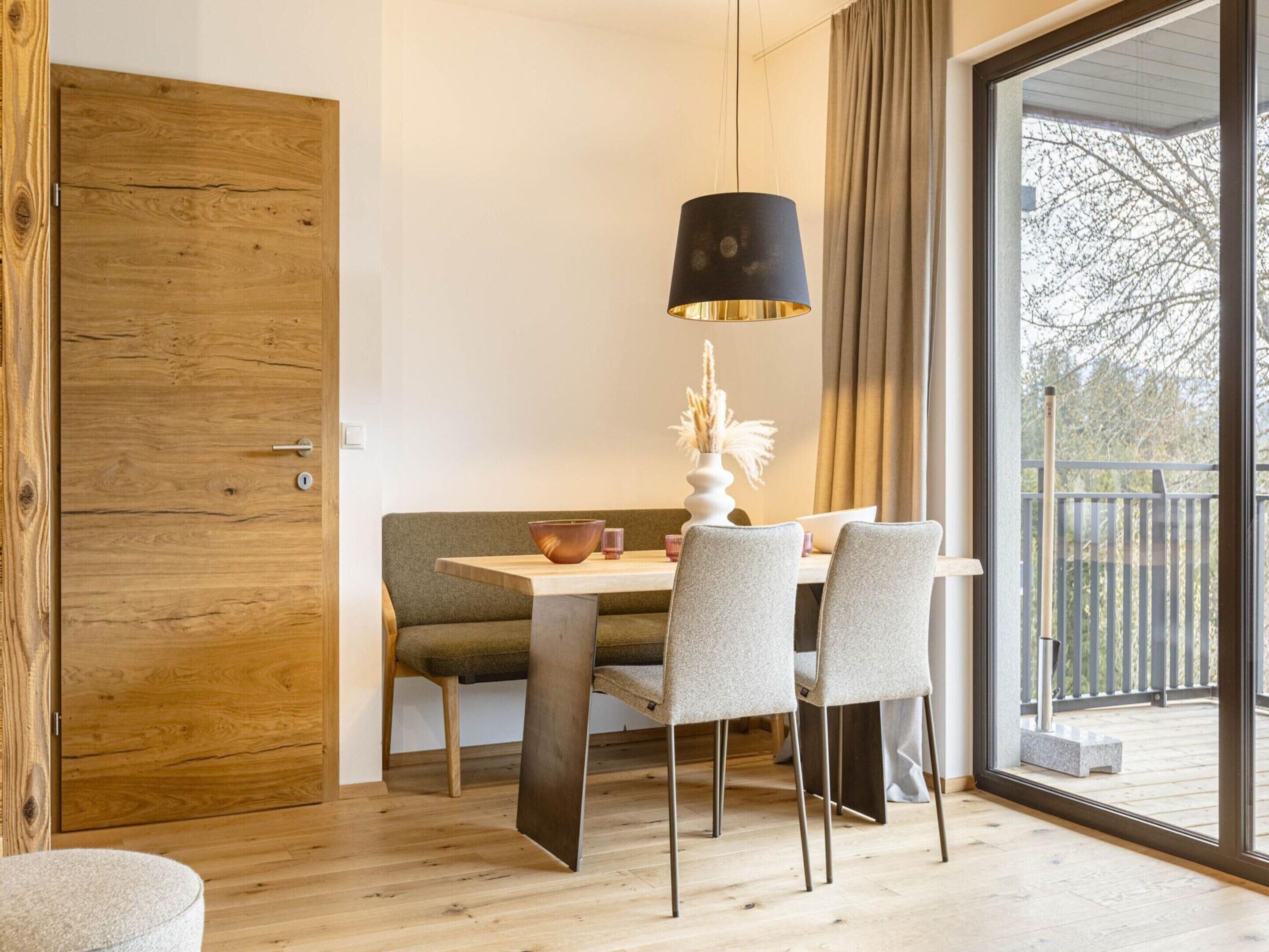 Ein Essbereich mit Holztür, Tisch mit Stühlen, einer Pendelleuchte und Blick ins Freie durch eine Glastür.
